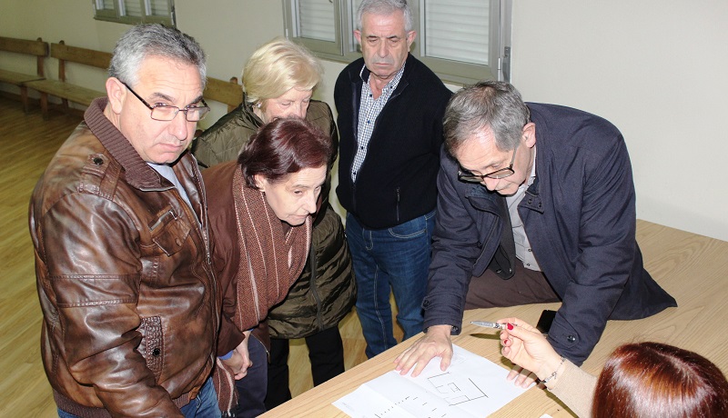 Un grupo de vecios/as, consultando o plano do centro social co alcalde